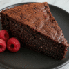 Slice of chia seed chocolate cake (no flour) on a black plate, showing a moist, fudgy crumb