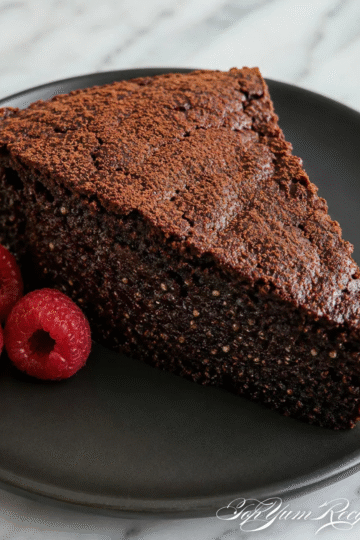 Slice of chia seed chocolate cake (no flour) on a black plate, showing a moist, fudgy crumb