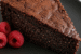 Slice of chia seed chocolate cake (no flour) on a black plate, showing a moist, fudgy crumb