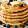 Fluffy lemon ricotta pancakes stacked on a plate with fresh berries, maple syrup, and powdered sugar.