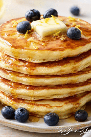 Fluffy lemon ricotta pancakes stacked on a plate with fresh berries, maple syrup, and powdered sugar.