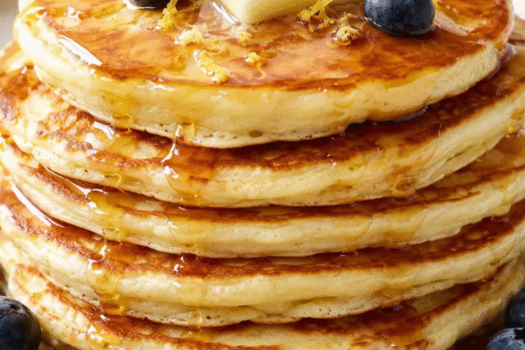 Fluffy lemon ricotta pancakes stacked on a plate with fresh berries, maple syrup, and powdered sugar.