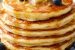 Fluffy lemon ricotta pancakes stacked on a plate with fresh berries, maple syrup, and powdered sugar.