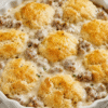 Sausage, Rich Gravy, and Biscuit Pie with golden biscuits baked over creamy sausage gravy