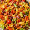 Frito taco salad with Catalina dressing in a large bowl, topped with corn chips, cheese, and ground beef
