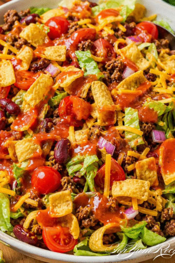 Frito taco salad with Catalina dressing in a large bowl, topped with corn chips, cheese, and ground beef