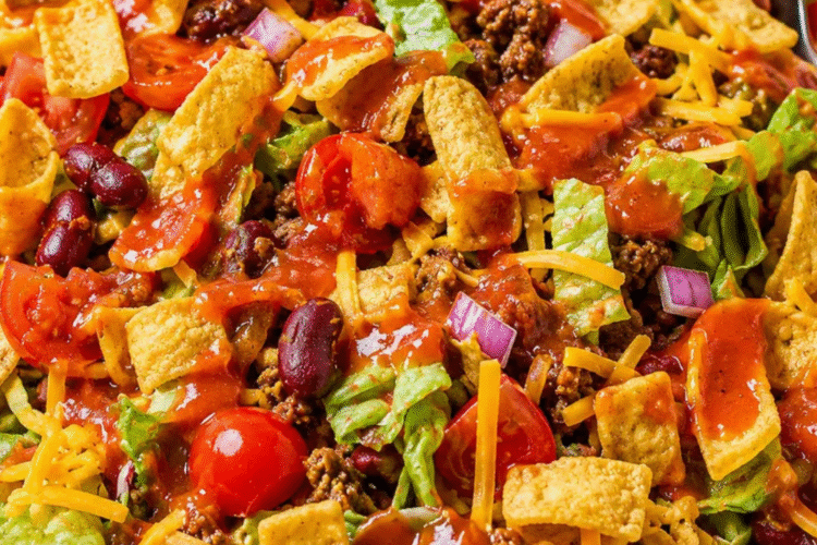 Frito taco salad with Catalina dressing in a large bowl, topped with corn chips, cheese, and ground beef